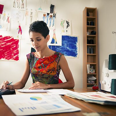 Money and financial planning, young hispanic self-employed woman checking bills and doing budget with calculator, computer and papers in fashion design studio
